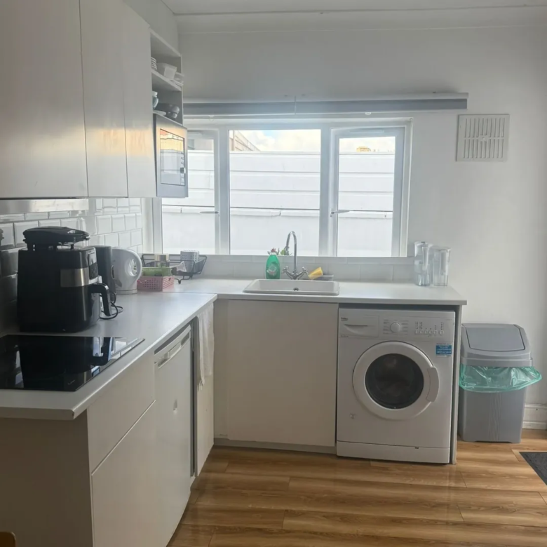 Bright kitchen with white cabinets, washing machine, sink and window.