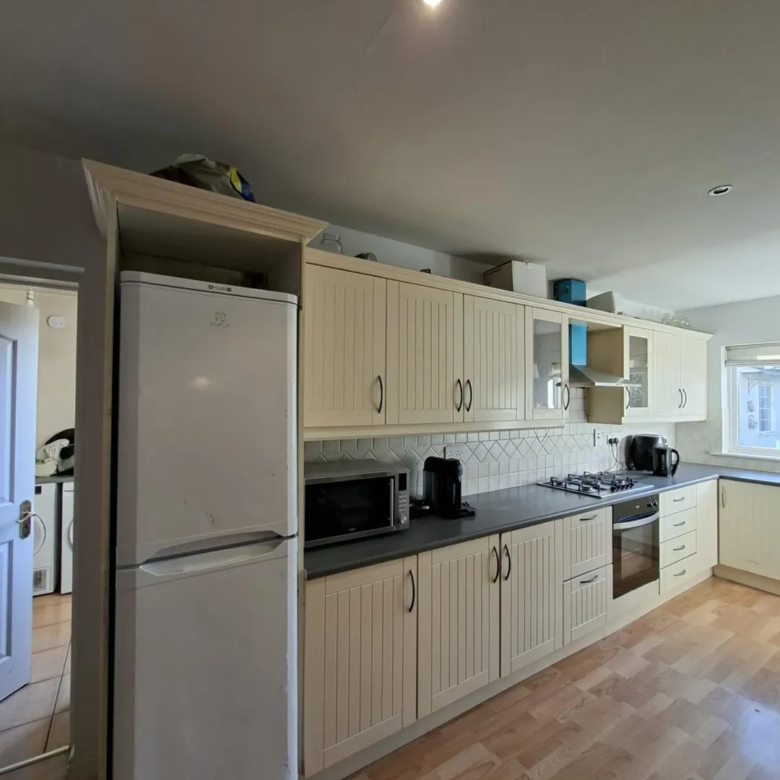 Kitchen with cream cabinets, grey countertop, fridge, microwave, and gas hob.
