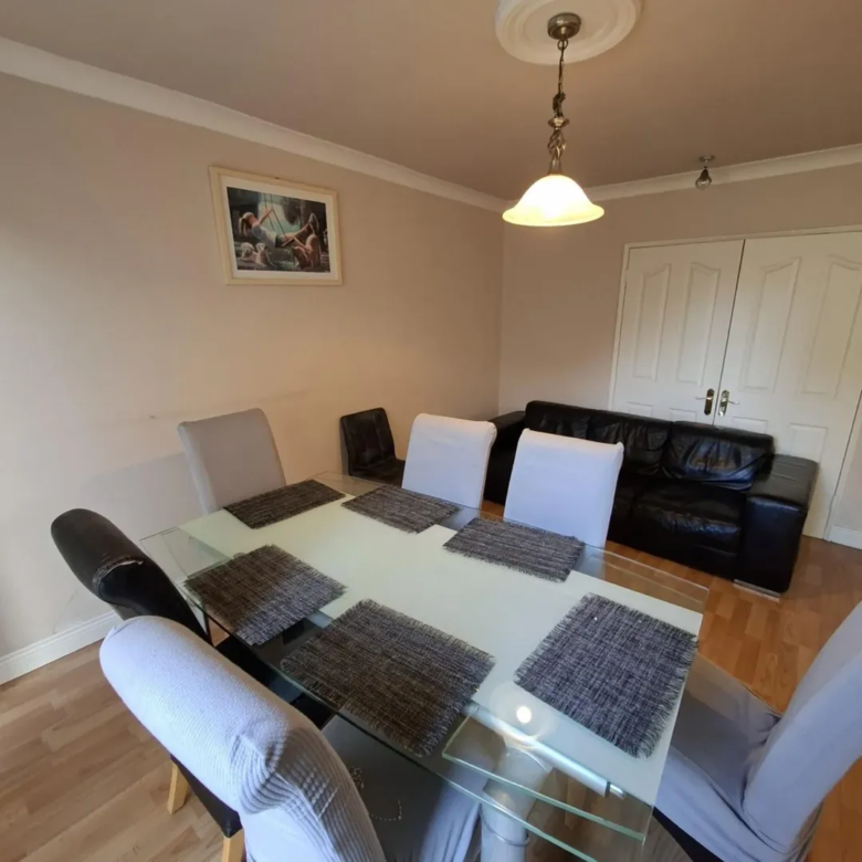 Dining room with glass table, chairs, and black leather sofa.