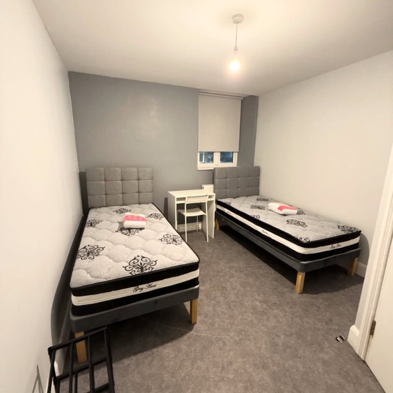 Dorm room with two twin beds, desk, and gray walls. Minimalist decor.