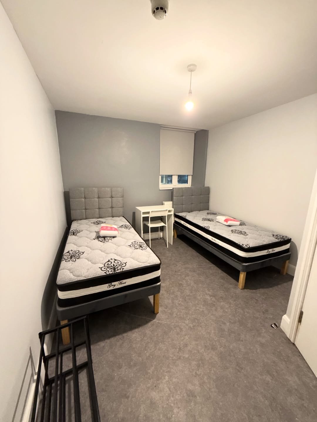 Dorm room with two twin beds, desk, and gray walls. Minimalist decor.