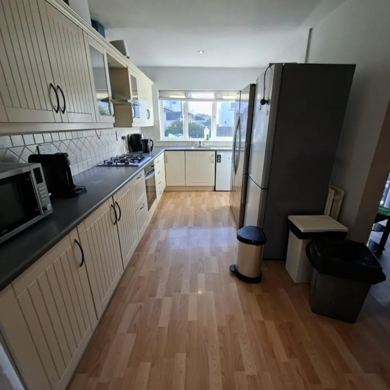 Galley kitchen with cream cabinets, dark countertops, and light wood flooring.