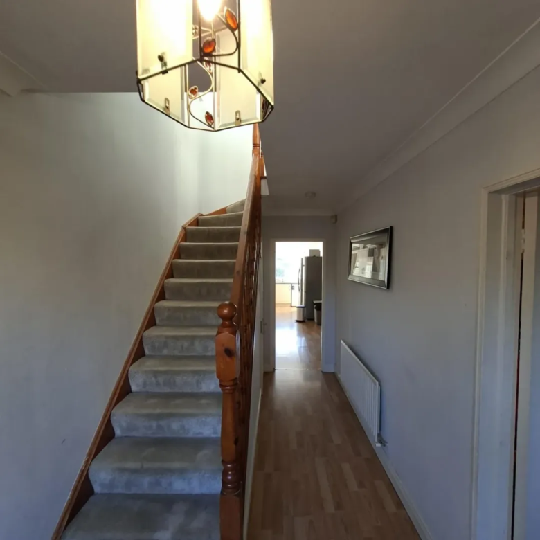 Hallway with carpeted stairs, wooden banister, and pendant light fixture.