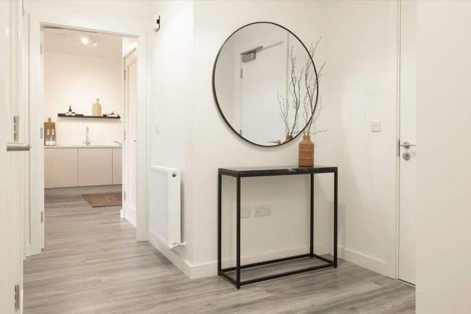 Hallway with console table, round mirror, and view into kitchen.