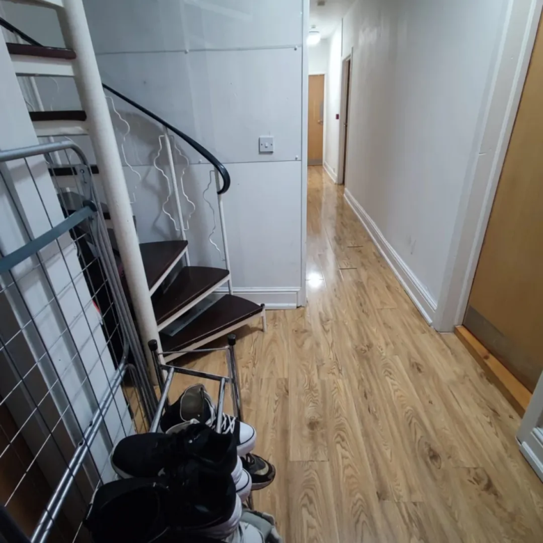 Hallway with stairs, shoe rack, and light wood flooring.