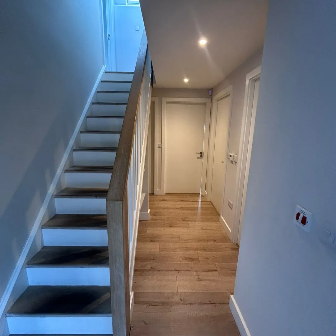 Hallway with stairs, wood floor, and white doors.
