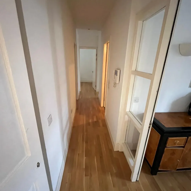 Hallway with wood flooring, white walls, and doorway view.