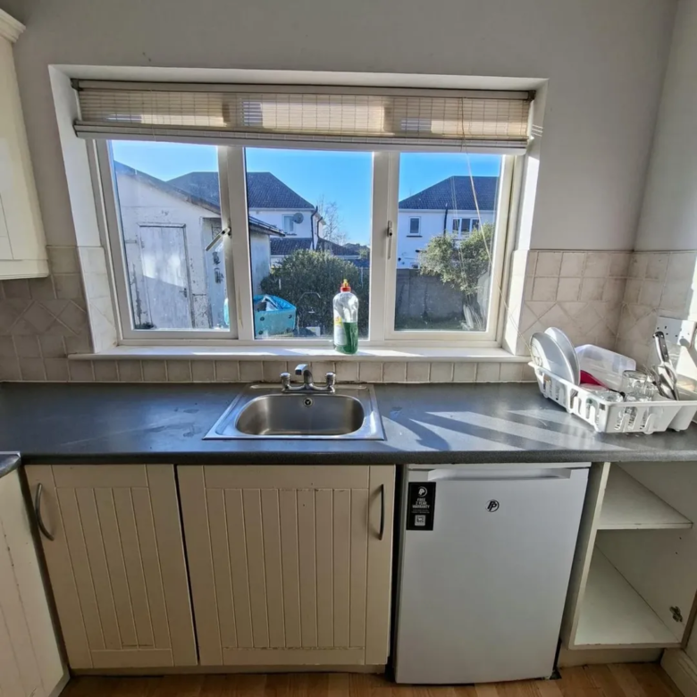Kitchen sink under window with dish soap and rack.