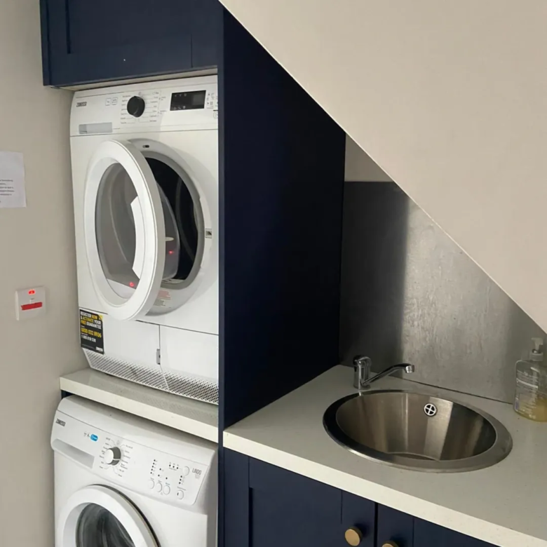 Laundry area with stacked washer dryer and sink in navy blue cabinetry.
