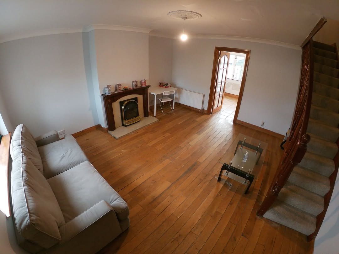 Living room with fireplace, sofa, table, and stairs. Hardwood floor.
