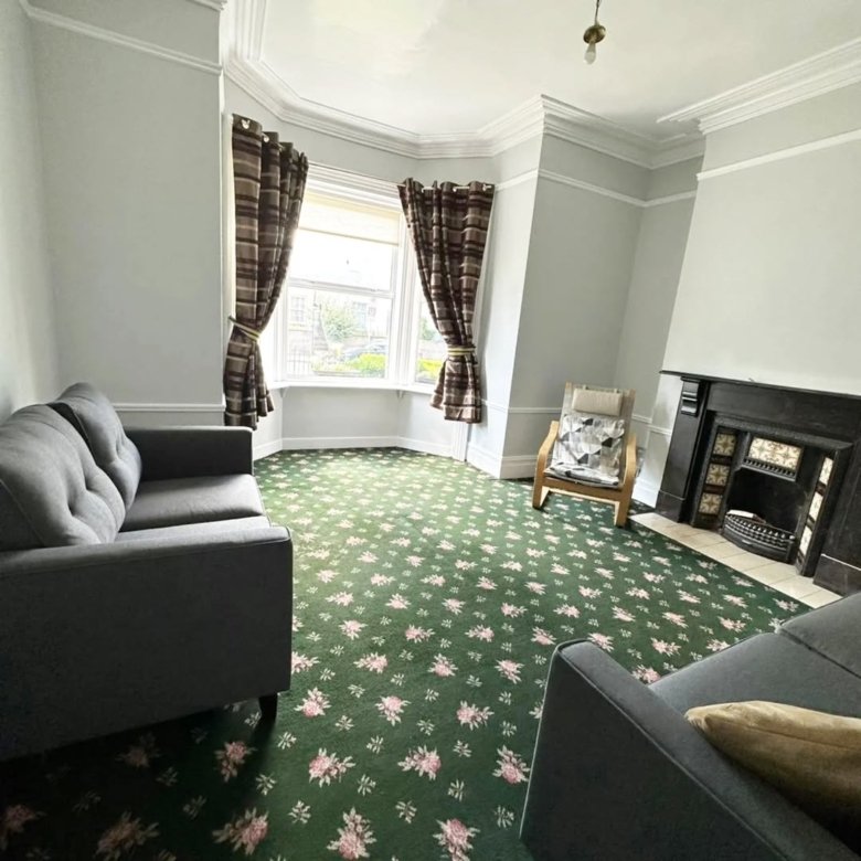 Living room with green floral carpet, gray sofa, bay window, and fireplace.