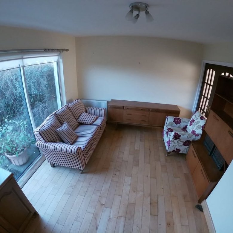Living room with striped sofa, floral armchair, and wooden furniture. Garden view through large window.