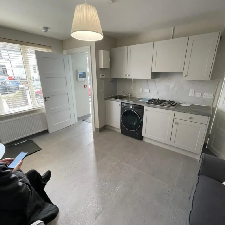 Modern apartment kitchen with white cabinets, washing machine, and window light.