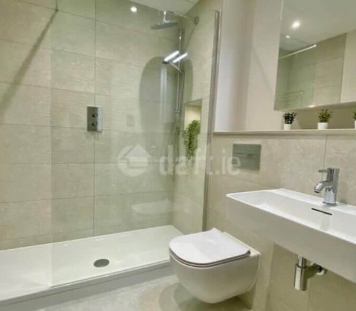 Modern bathroom with walk-in shower, toilet, and sink. Neutral tile and minimalist design.