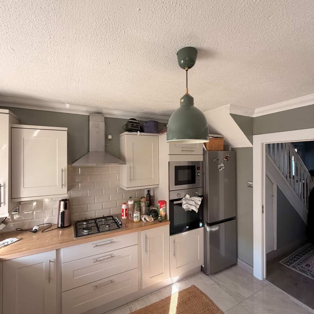 Modern kitchen with gray cabinets, stainless steel appliances, and a green pendant light.