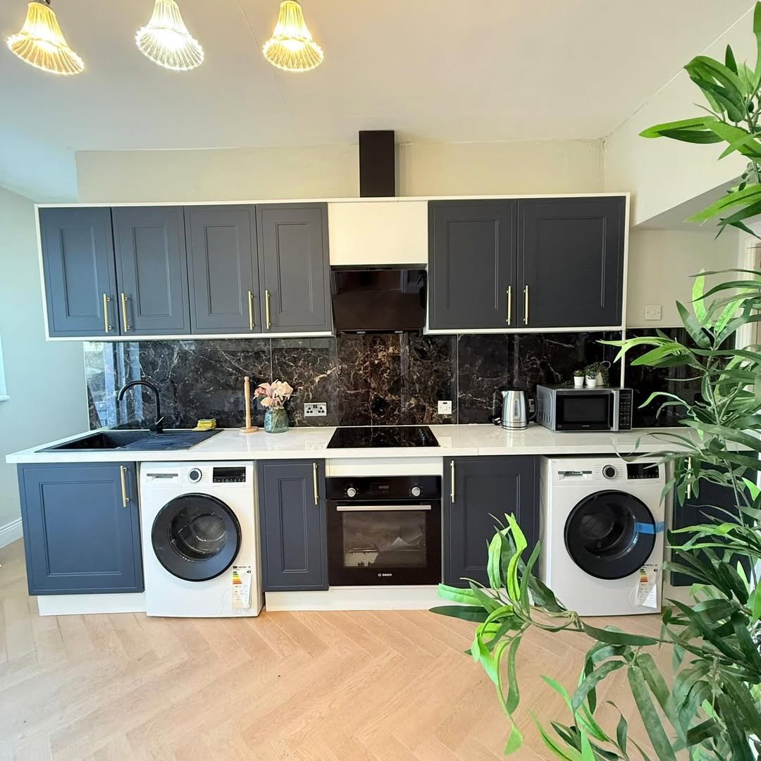 Modern kitchen with dark blue cabinets, white countertops, and black marble backsplash.