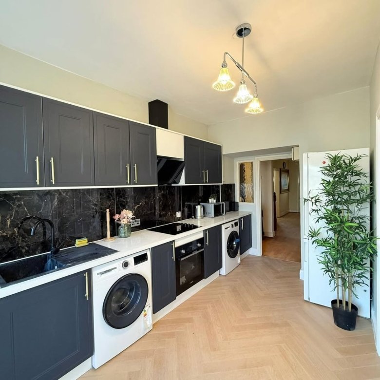Modern kitchen with dark cabinets, herringbone floor, washing machine, and indoor plant.