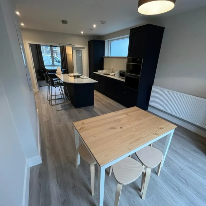 Modern kitchen with island, dining table, and stools. Gray floors.