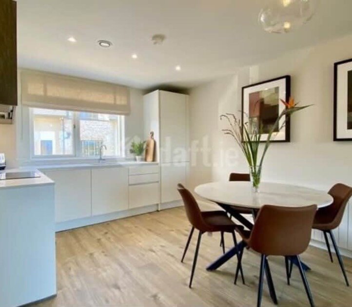 Modern kitchen with white cabinets, dining table, and brown chairs.