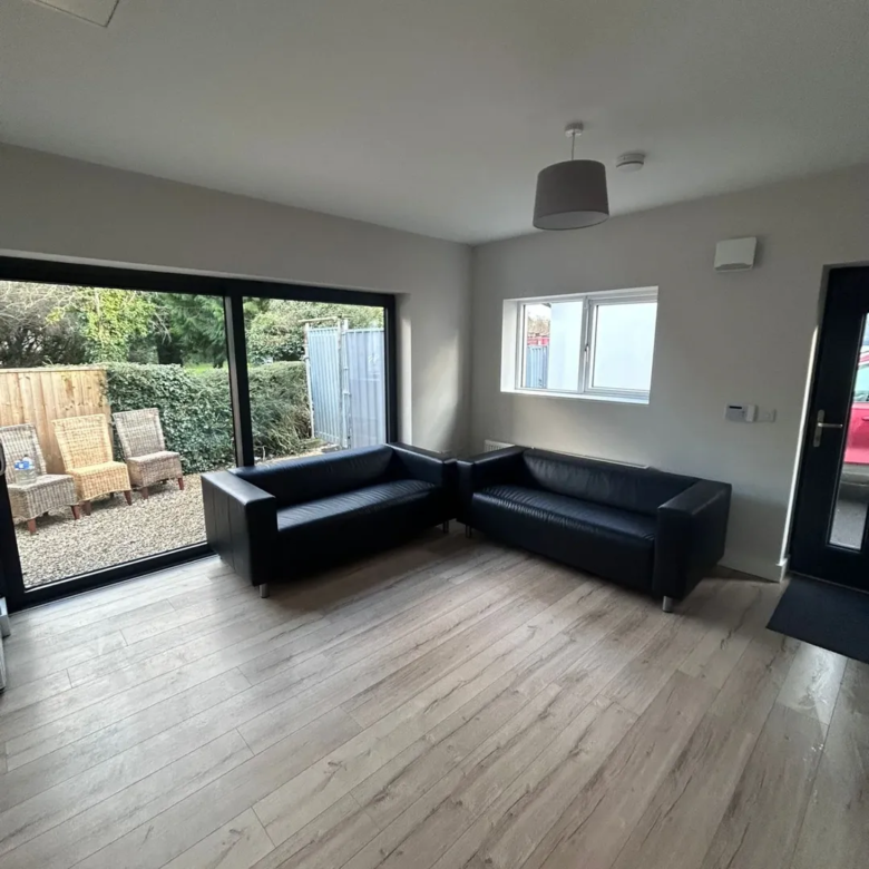 Modern living room with black sofas, wood floors, sliding glass doors, and outdoor seating area.