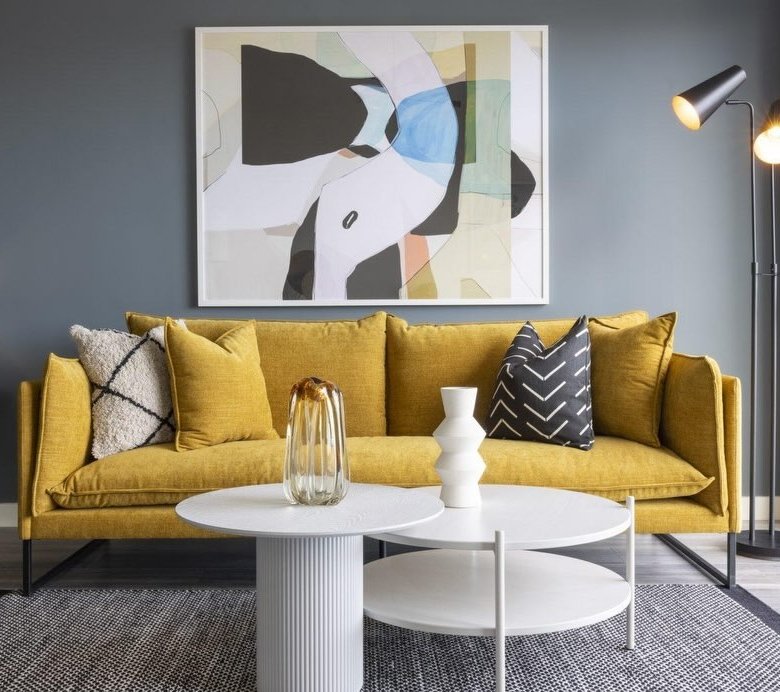 Modern living room with yellow sofa, abstract art, and white coffee tables.