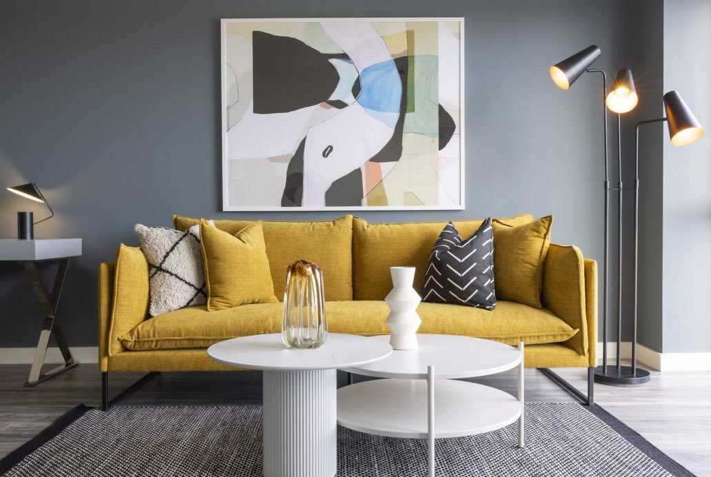 Modern living room with yellow sofa, abstract art, and white coffee tables.