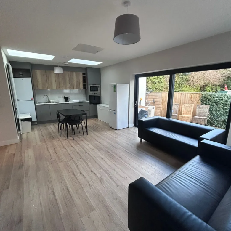 Modern open-plan living space with black sofa, dining table, and kitchen area under skylights.
