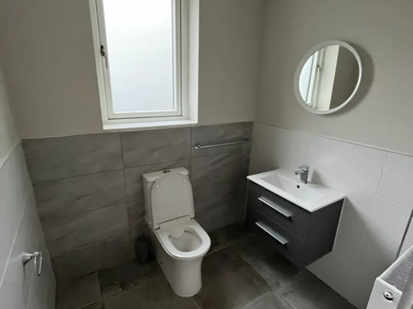 Small modern bathroom with toilet, sink, and round mirror.