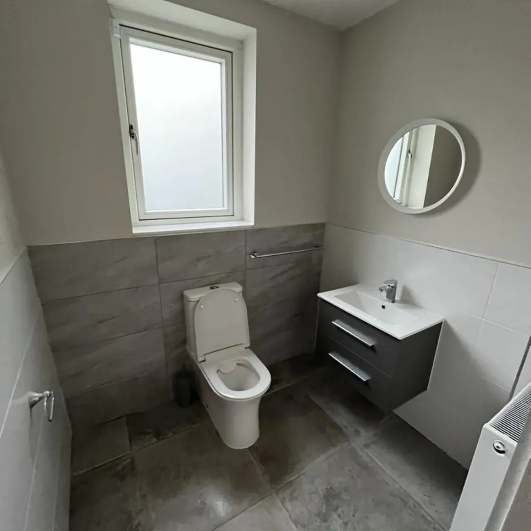 Small modern bathroom with toilet, sink, and round mirror.