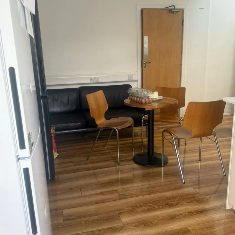 Small office break room with table, chairs, and black sofa.
