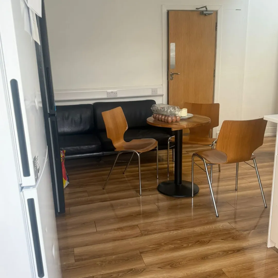 Small office break room with table, chairs, and black sofa.