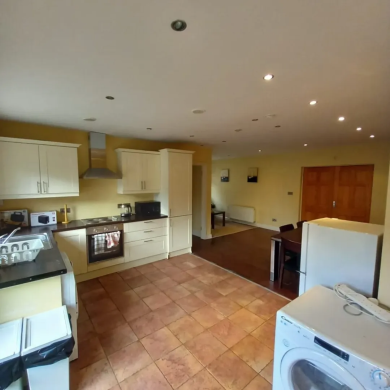 Open-plan kitchen with cream cabinets, terracotta floor, and appliances.