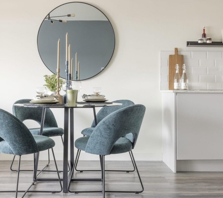 Round dining table with blue chairs and a round mirror on the wall.