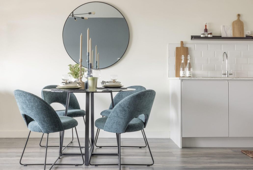 Round dining table with blue chairs and a round mirror on the wall.