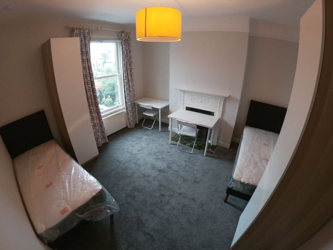Shared bedroom with two beds, desks, wardrobes, gray carpet, and a yellow lampshade.
