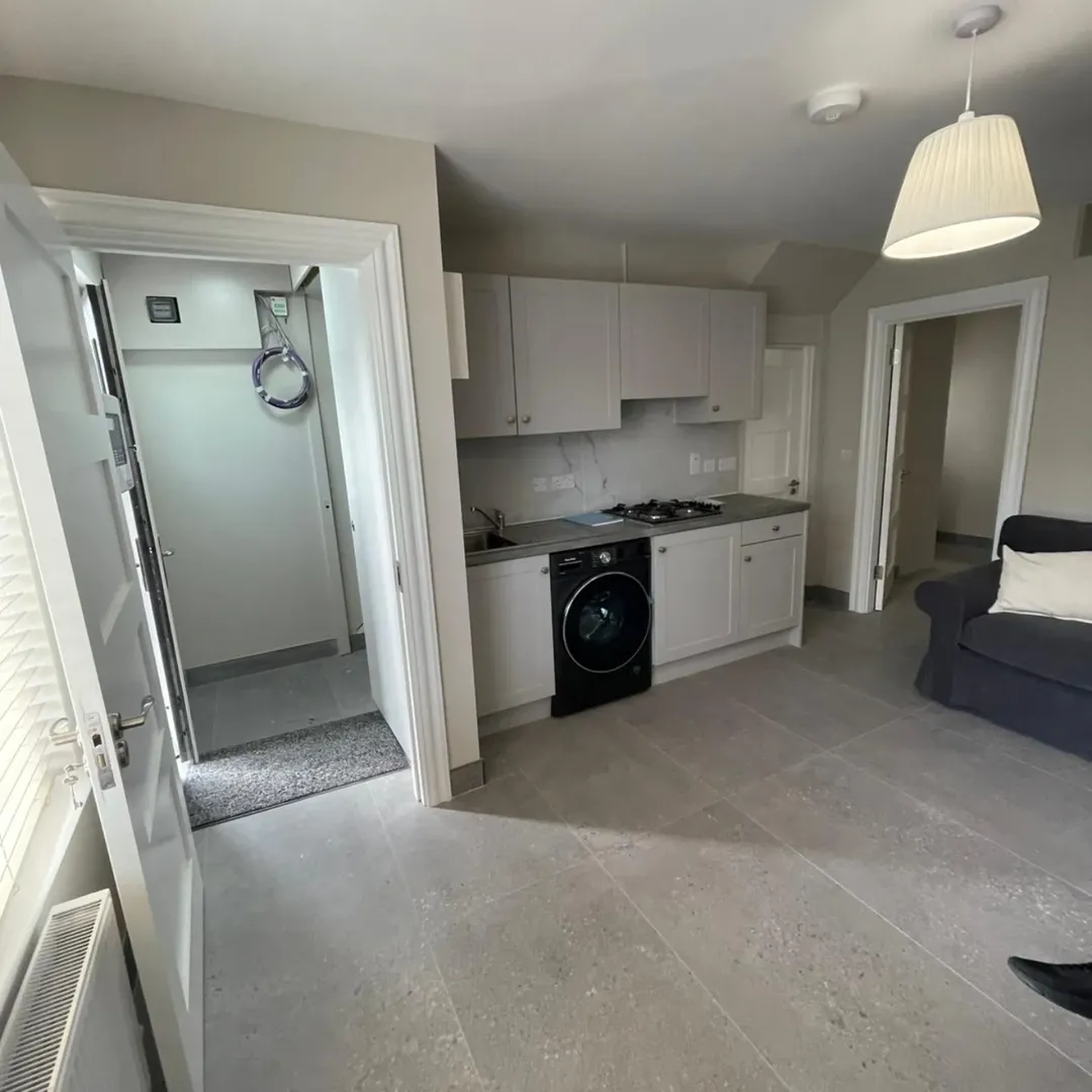 Small apartment kitchen with washer, light gray cabinets, and doorway to bathroom.
