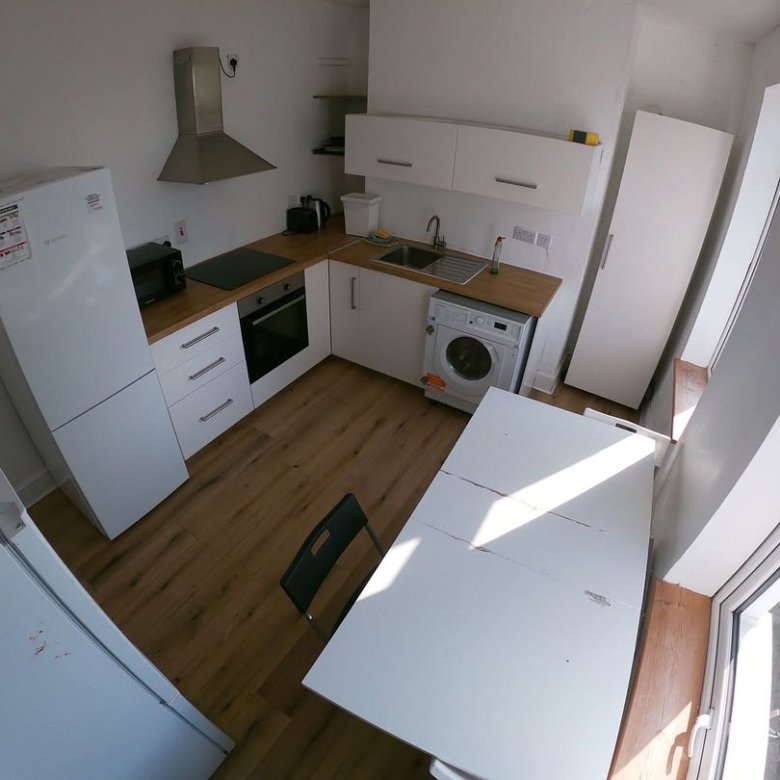 Compact kitchen with white cabinets, appliances, table, and chair in a small apartment.