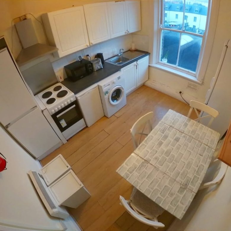 Compact kitchen with white cabinets, appliances, dining table, and chairs in a small apartment setting.
