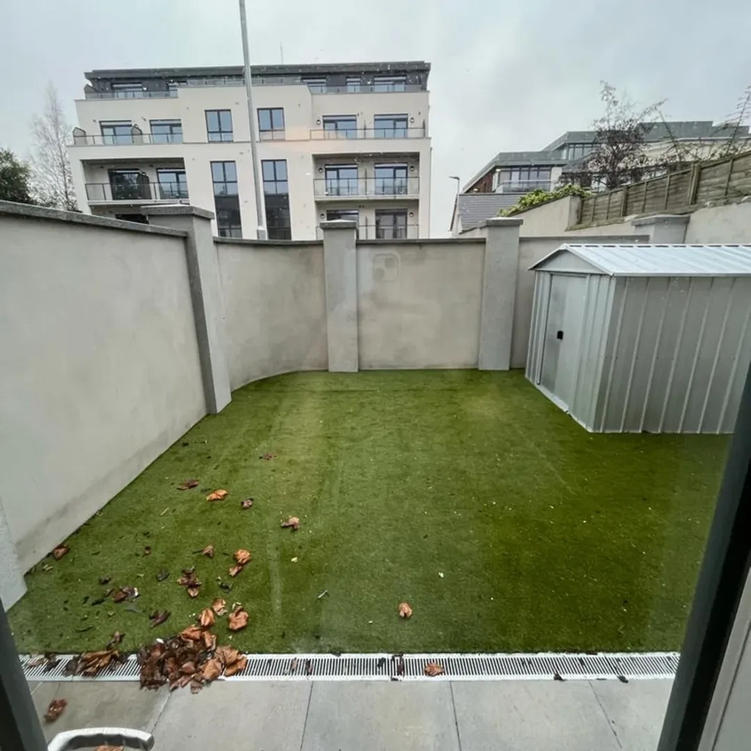 Small backyard with artificial grass, shed, and surrounding walls.