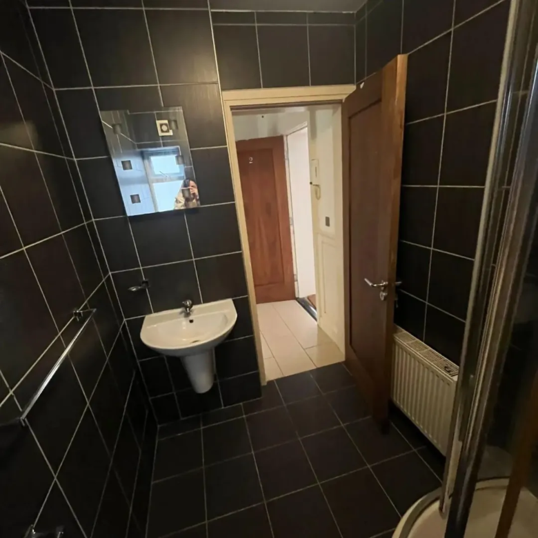 Small bathroom with dark tiles, sink, mirror, and open door.