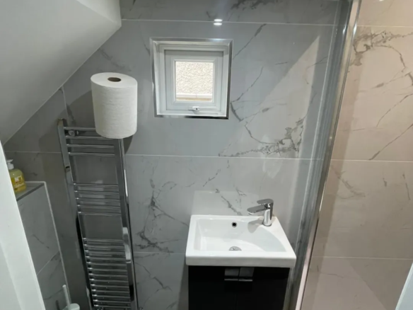Small bathroom with gray marble tiles, sink, towel warmer, and toilet.