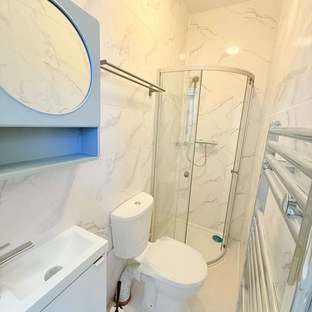 Small bathroom with marble tiles, shower, toilet, sink, and towel warmer.