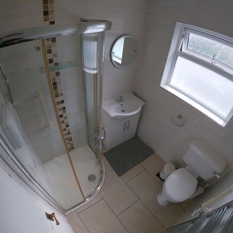 Small bathroom with shower, toilet, sink, and window. Neutral tile.