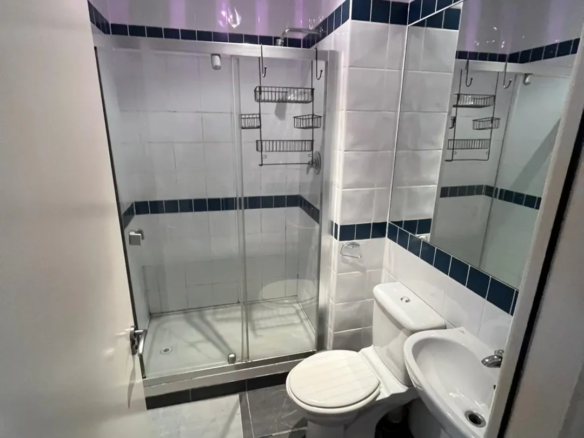 Small bathroom with shower, toilet, sink, and gray tile floor.