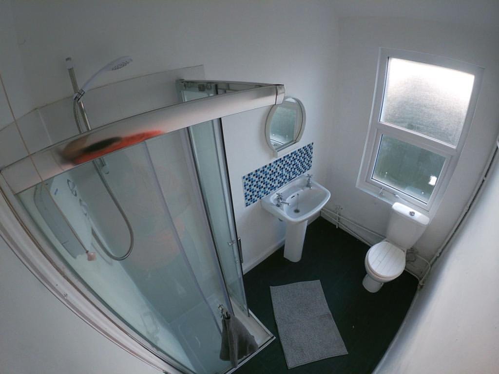 Small bathroom with shower, toilet, sink, and window. Dark floor.
