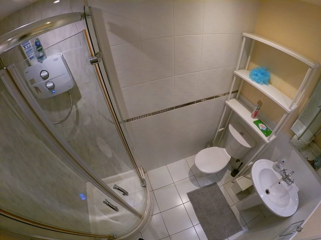 Compact bathroom with shower, toilet, sink, and storage shelf.