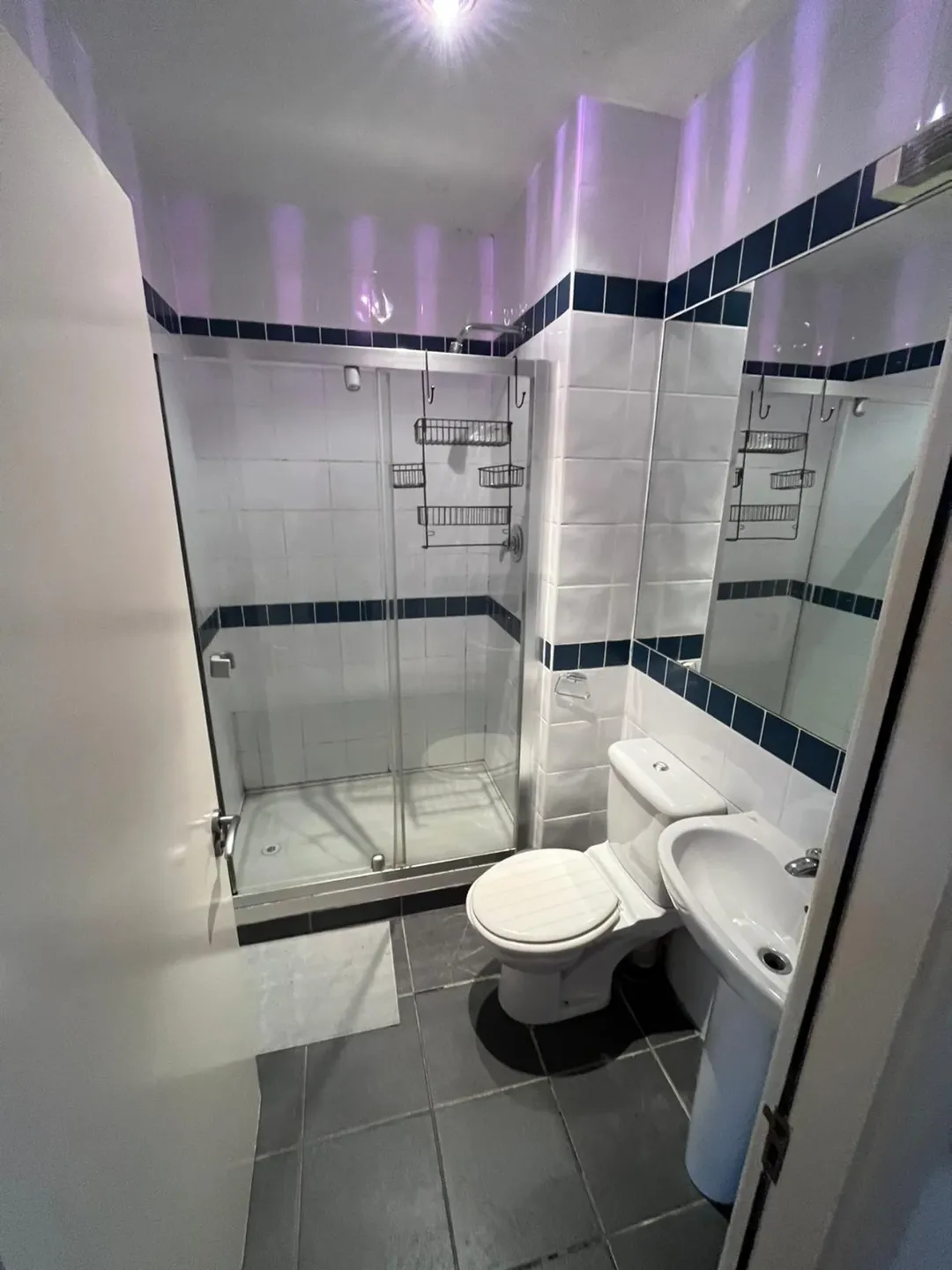 Small bathroom with shower, toilet, sink, and gray tile floor.