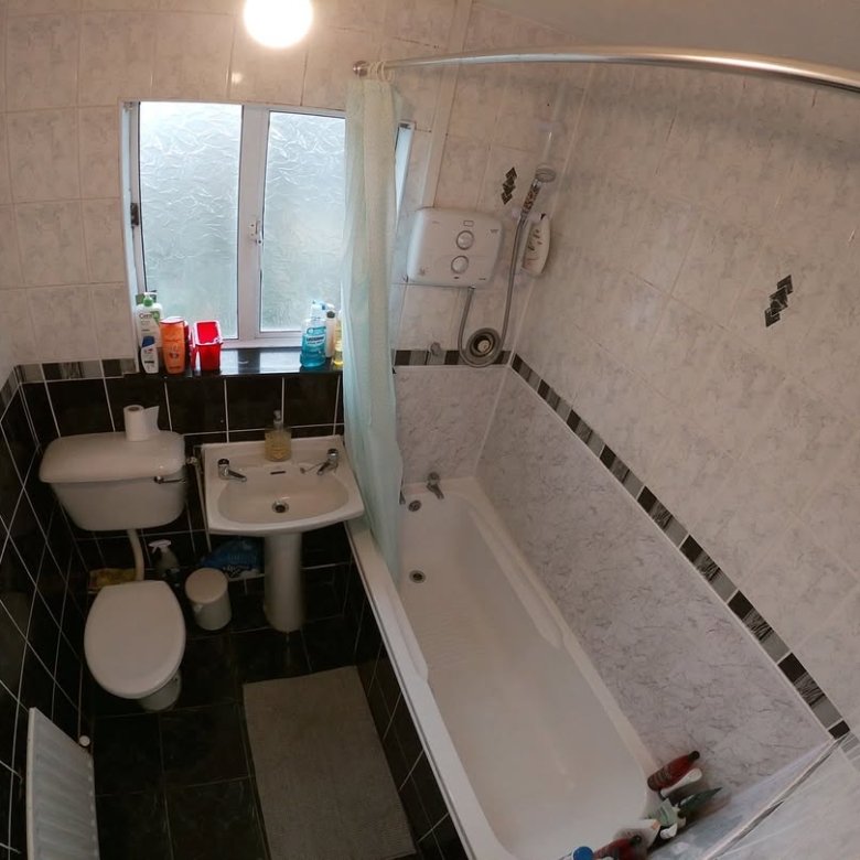 Small bathroom with toilet, sink, bathtub, shower curtain, and tiled walls.