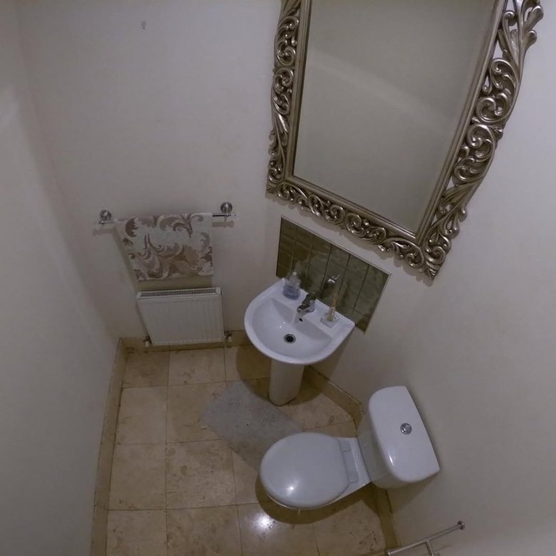 Small bathroom with toilet, sink, ornate mirror, and beige tile floor.