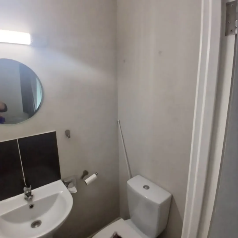 Small bathroom with toilet, sink, mirror, and neutral color scheme.